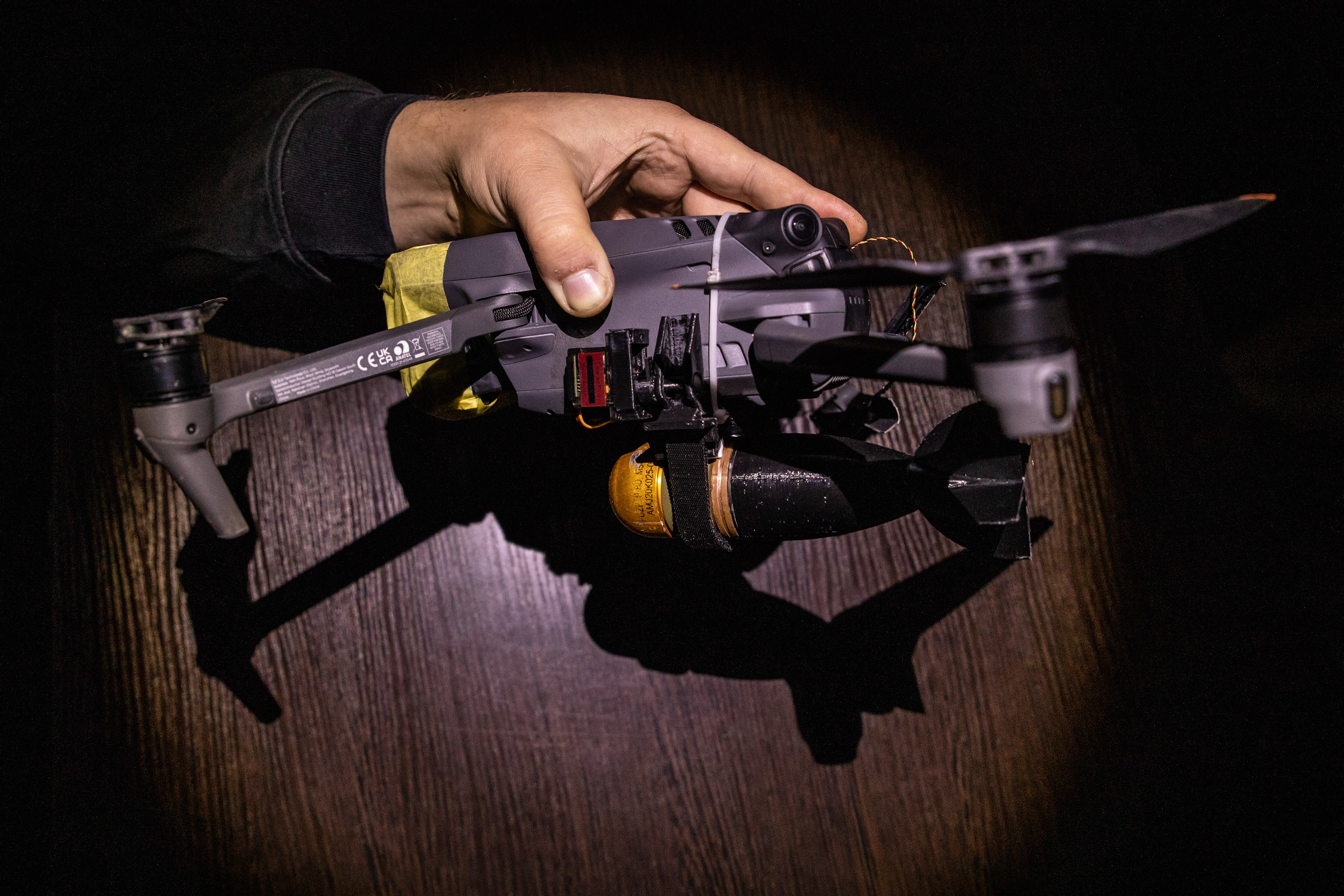 Hand holds a small quadcopter drone with a bomblet attached.