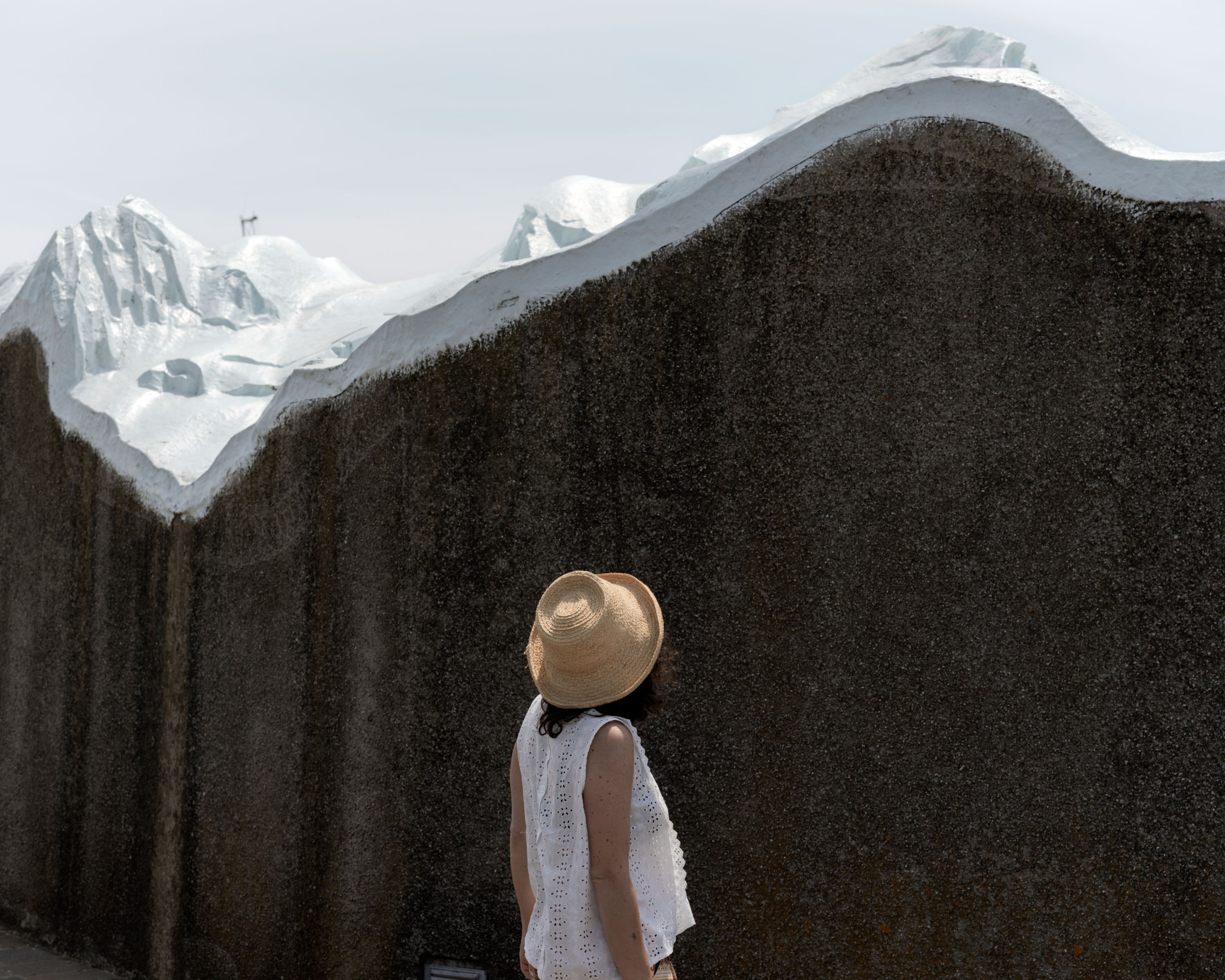the back of a woman in a sun hat standing next to an artificial snow wall
