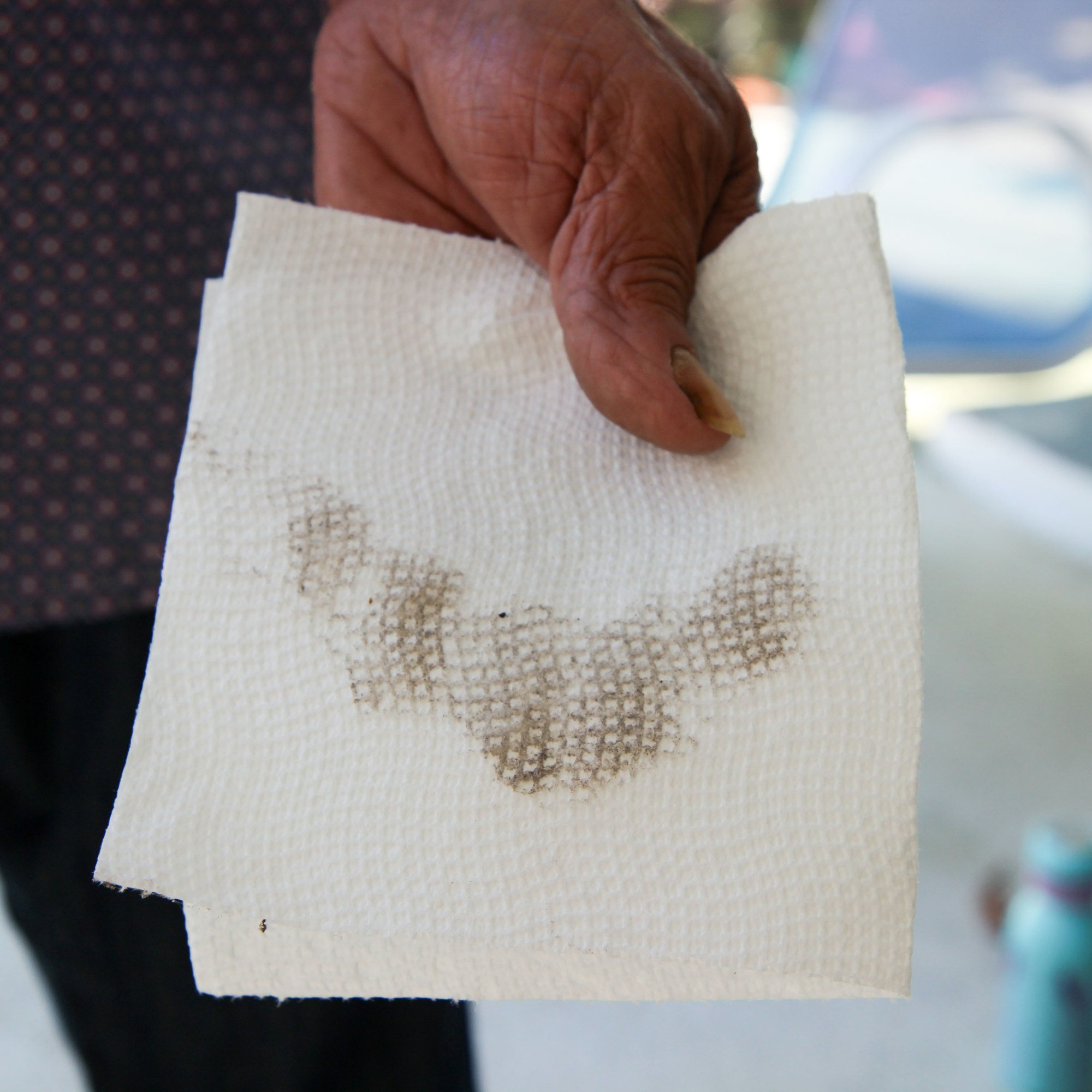 close up of a hand holding a paper towel with a gritty black streak on it